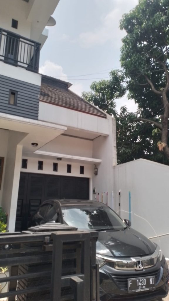 Tampilan depan rumah dua lantai bergaya modern dengan mobil terparkir di carport, sebelum pemasangan kanopi pelindung area parkir.