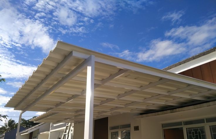Kanopi atap Alderon Single Layer berwarna putih dengan rangka besi hollow putih terpasang di depan rumah minimalis di bawah langit cerah.