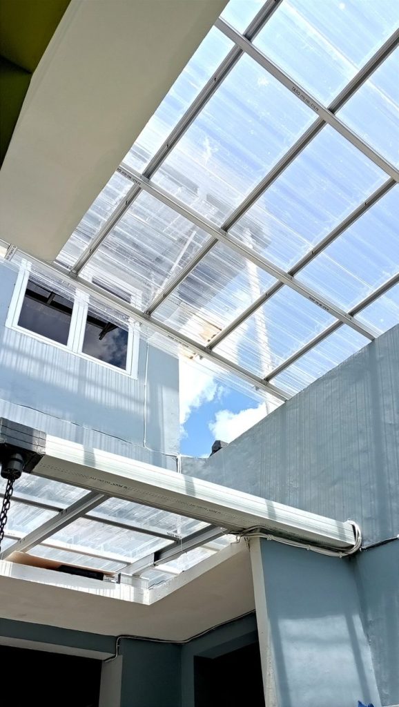 Kanopi polikarbonat transparan terpasang di atap rumah modern, memungkinkan cahaya alami masuk ke area dalam tanpa mengorbankan perlindungan cuaca.