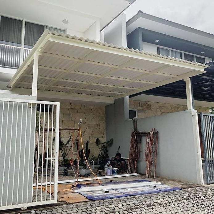 Kanopi atap Alderon Double Layer dengan rangka besi hollow putih dipasang di garasi rumah modern, terlihat proses pengerjaan masih berlangsung.