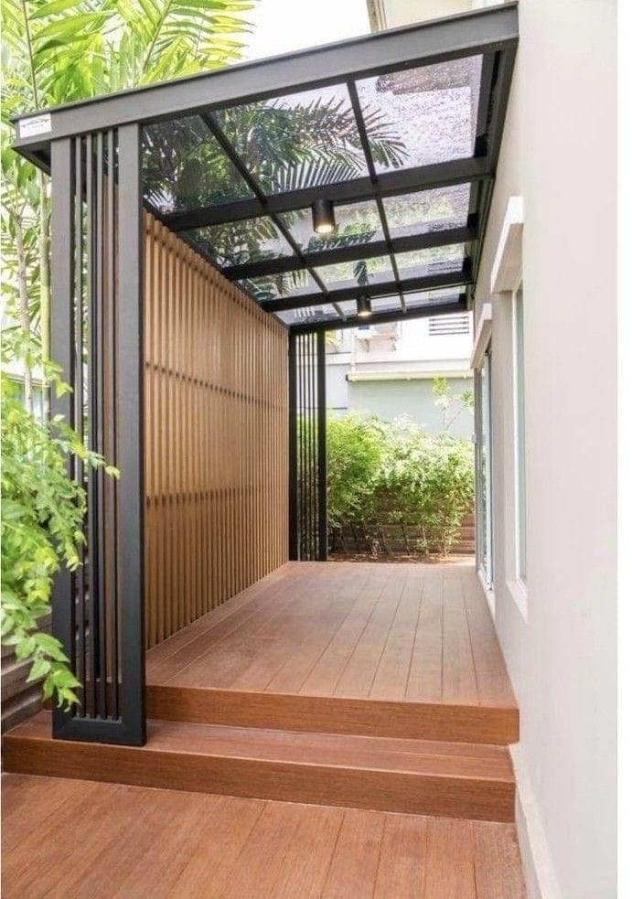Desain kanopi minimalis modern dari bengkel kanopi dengan struktur besi hitam dan atap kaca, terpasang di samping rumah dengan lantai kayu elegan.