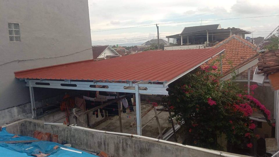 Kanopi atap spandek pasir warna merah dengan rangka baja ringan di area jemuran rumah padat penduduk, efektif meredam suara hujan.