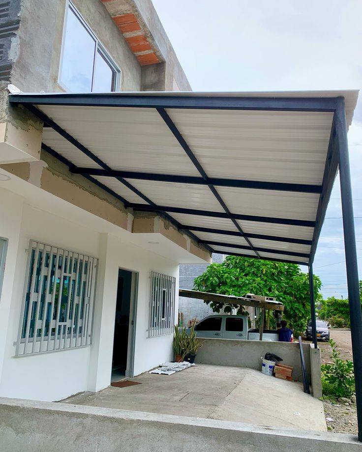 Kanopi rumah minimalis dengan rangka besi hitam dan atap spandek berwarna putih, terpasang di halaman depan rumah modern dua lantai.